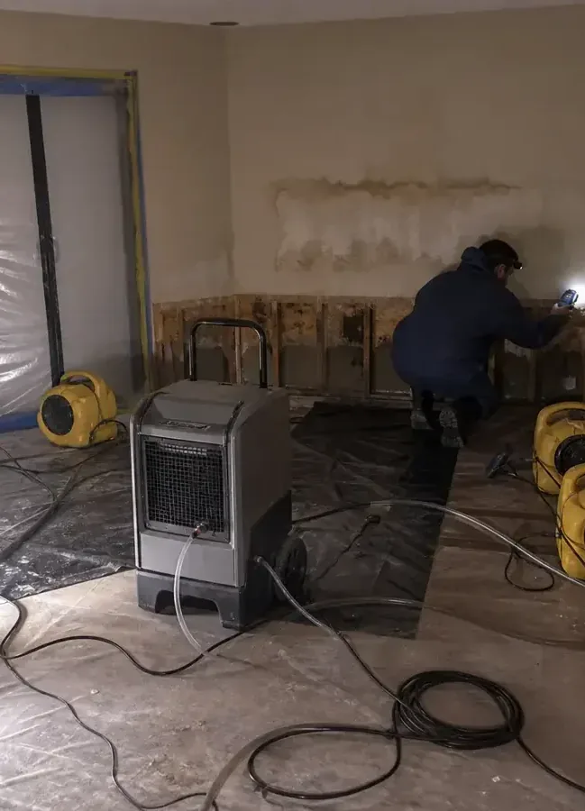 Technician checking an opened wall beside drying equipment