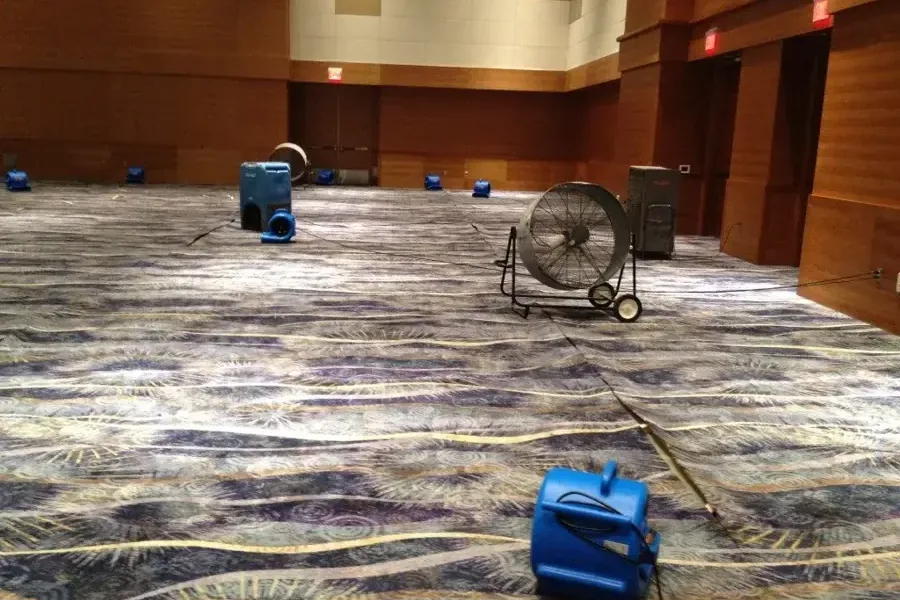 Air movers drying carpet inside a large event hall